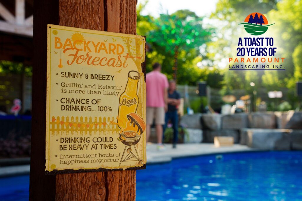 Close-up of a humorous “Backyard Forecast” sign by the pool area at Paramount Landscaping’s 20th Anniversary Celebration, with the event logo in the background.