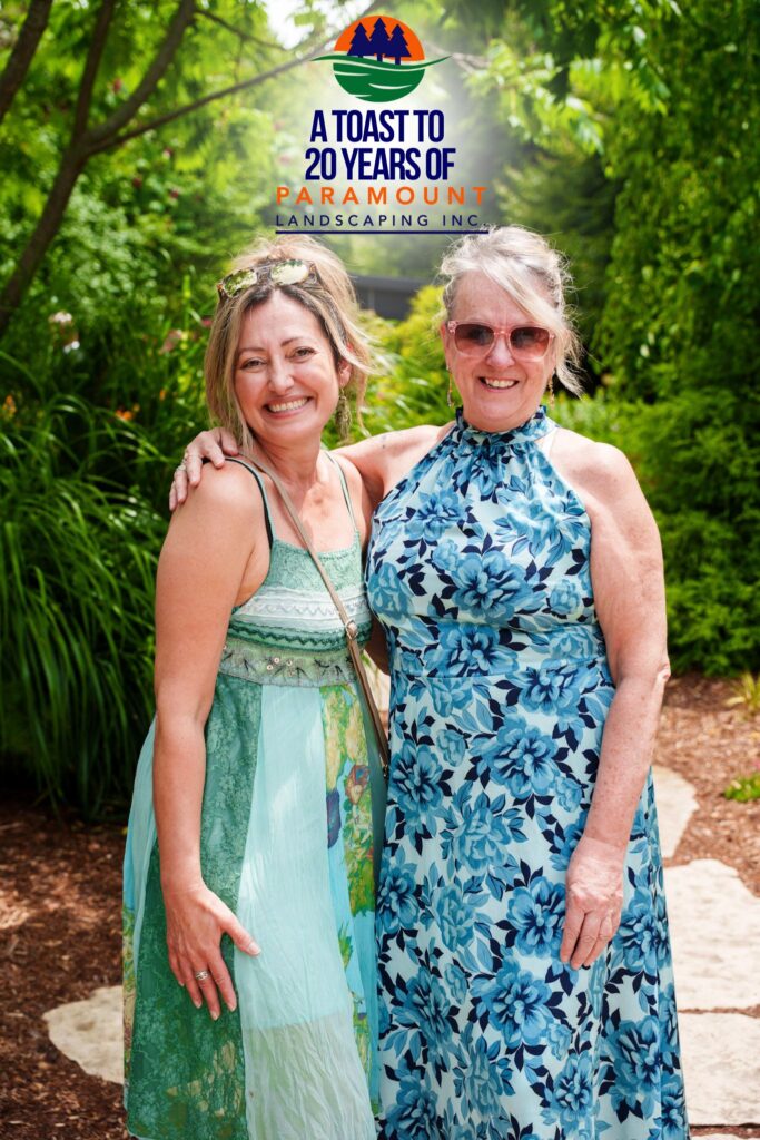 Two guests smiling together in front of a lush green backdrop at Paramount's 20th Anniversary event.