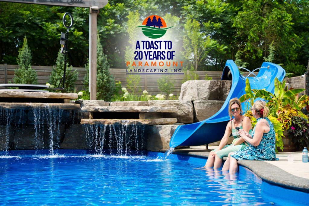 Two women in a blue floral dress lounges by the pool under the Paramount Landscaping 20th Anniversary archway.