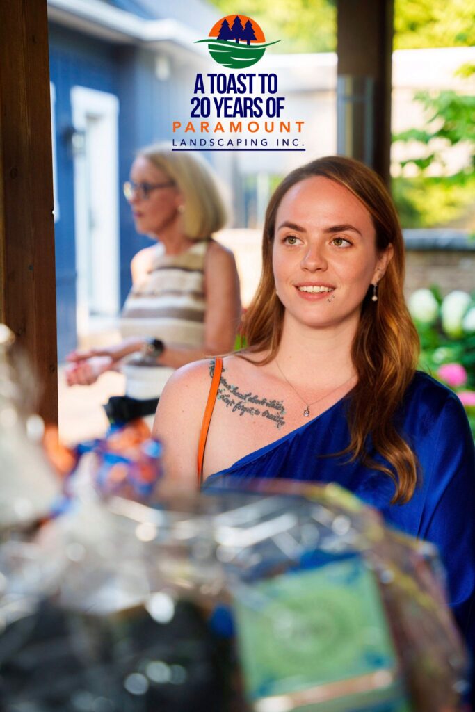Melissa Rolston handing out giveaway prizes at the Paramount Landscaping 20th Anniversary celebration, with Peggi Shepherd DeGroote visible in the background.