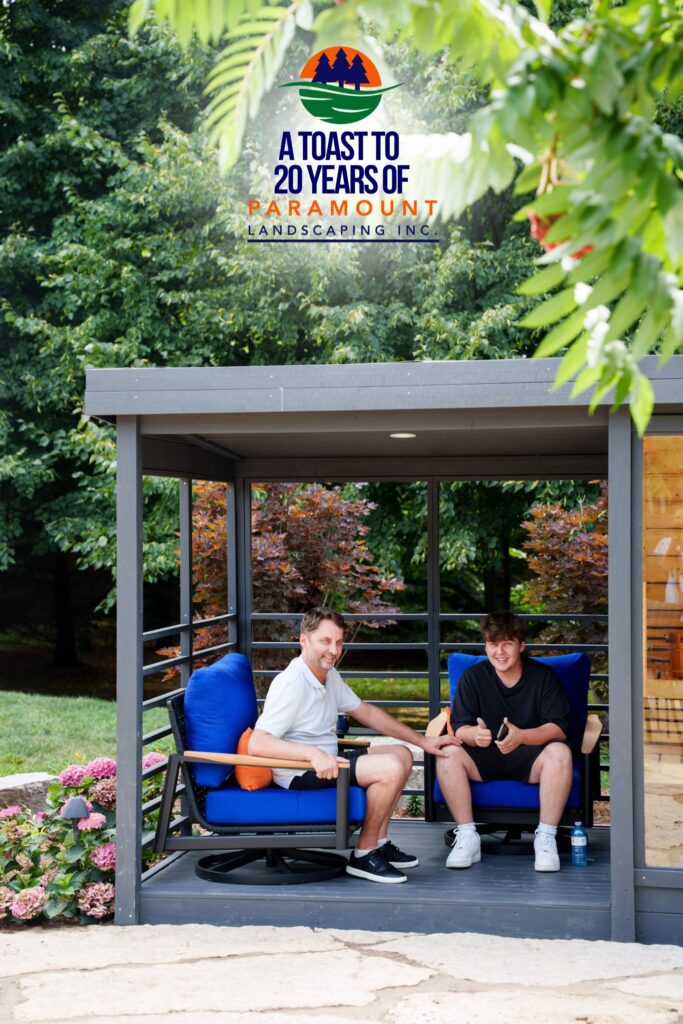 Anthony, owner of Pro Patio Furniture, sitting with his son on one of their furniture pieces beside Paramount Landscaping’s custom-built outdoor sauna at the 20th anniversary celebration.