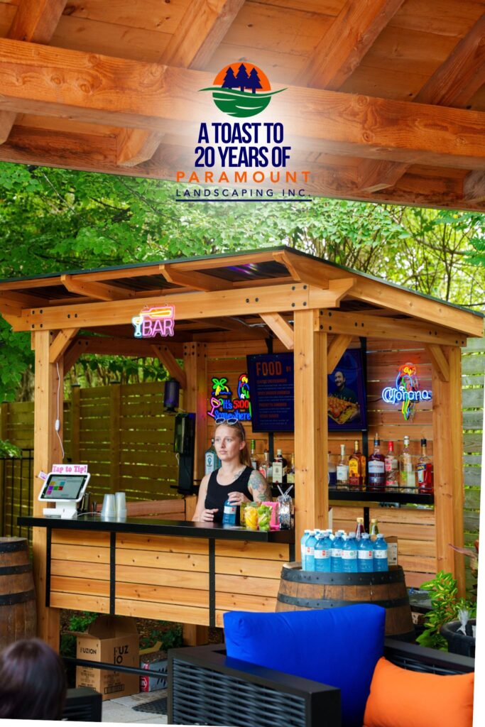 A bartender from Two Hot Blondes Bartending Service smiling behind a wooden bar setup at Paramount Landscaping’s 20th Anniversary event.