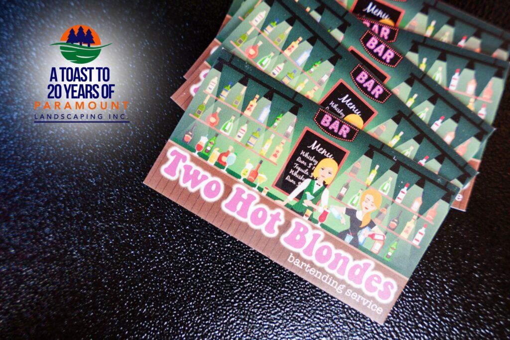 Flyer for Two Hot Blondes Bartending Services displayed on a wooden bar at Paramount Landscaping’s 20th Anniversary event.